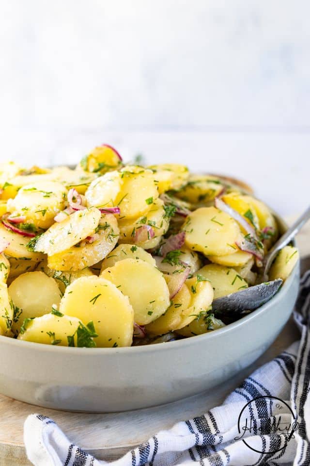 German Potato Salad with a large spoon in the bowl in a white serving bowl.