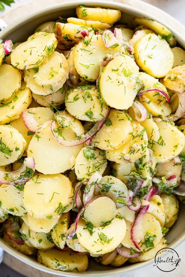 German potato salad in a large bowl with fresh dill on top.