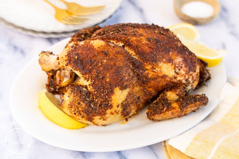 Cooked rotisserie chicken on a white platter with forks pictured.