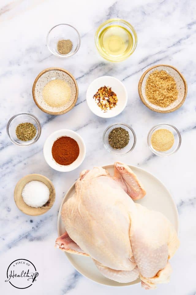 Ingredients for an oven-roasted rotisserie chicken on a marble background in separate containers.
