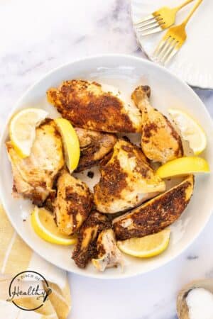 A cut up roasted rotisserie chicken on a white serving platter with lemon slices