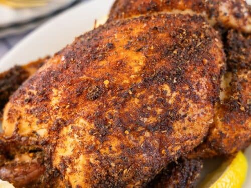 Roasted Rotisserie Chicken with lemon slices on a white platter.