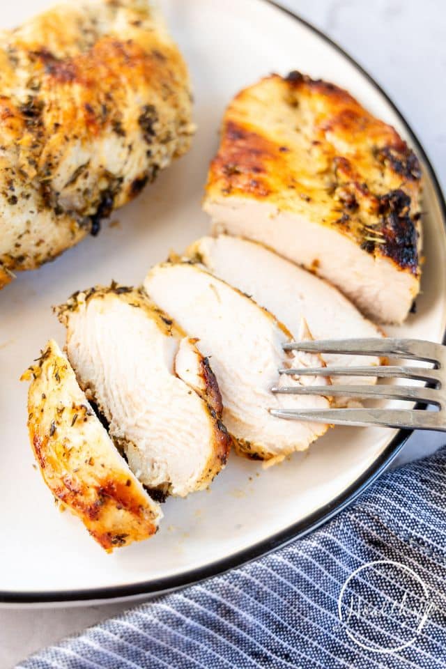 Sliced, cooked marinated chicken on a white plate with a fork.