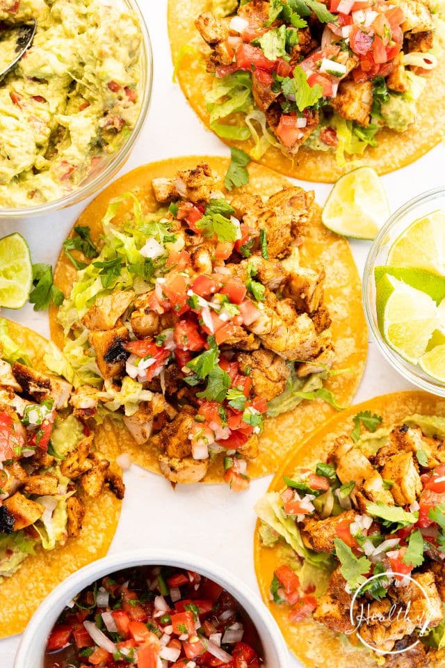 A platter of grilled chicken street tacos layed out with quartered limes in a bowl.