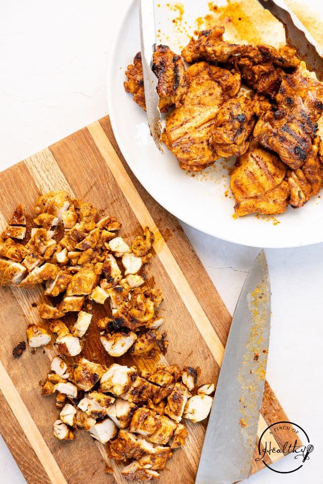 Chicken for street tacos being chopped into bite-sized pieces on a cutting board.
