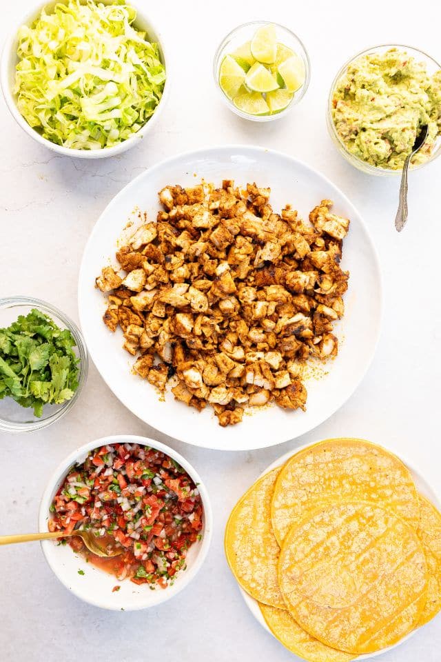 Diced chicken with the rest of the ingredients for grilled chicken street tacos in separate containers on a white background.