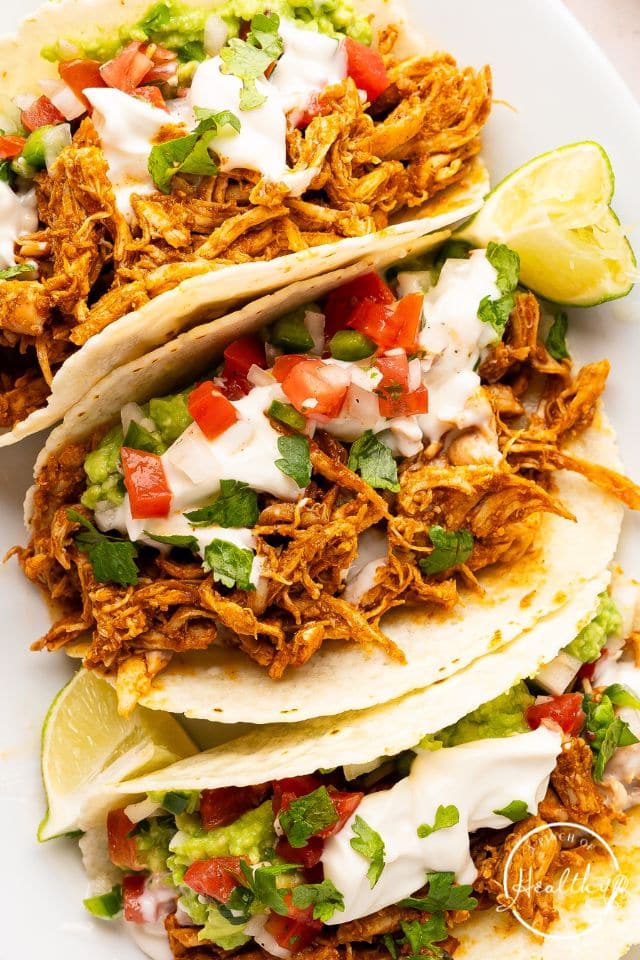 Three shredded chicken tacos with toppings.