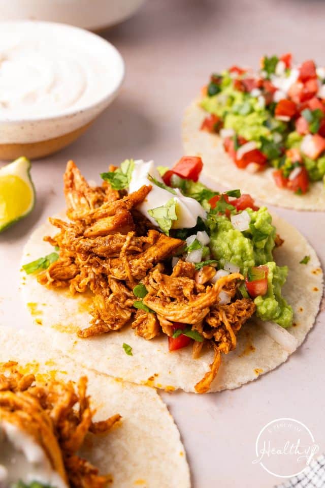 A shredded chicken taco on a flour tortilla topped with guacamole, sour cream, and tomatoes.