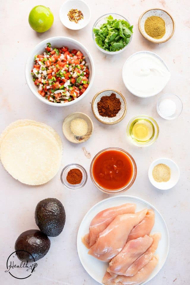 Ingredients for shredded chicken tacos in separate containers on a white background.