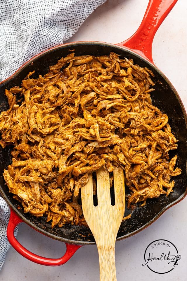 Shredded chicken tacos in a skillet after being sauced and seasoned.