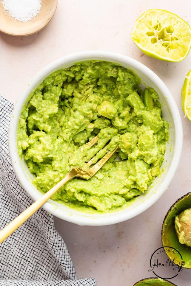 Guacamole in a white bowl with a fork inside the bowl.