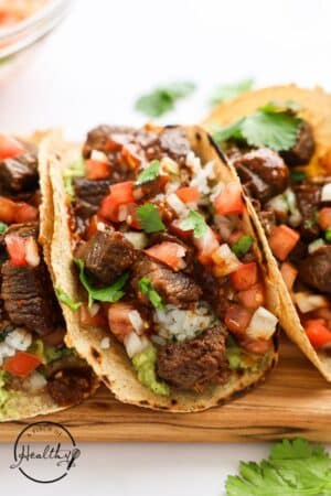 Steak tacos on a wooden cutting board with tomatoes.