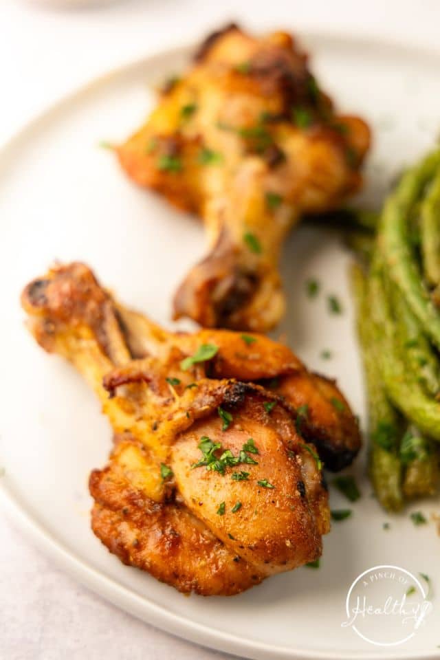 Butterflied chicken legs with green beans on a white plate.
