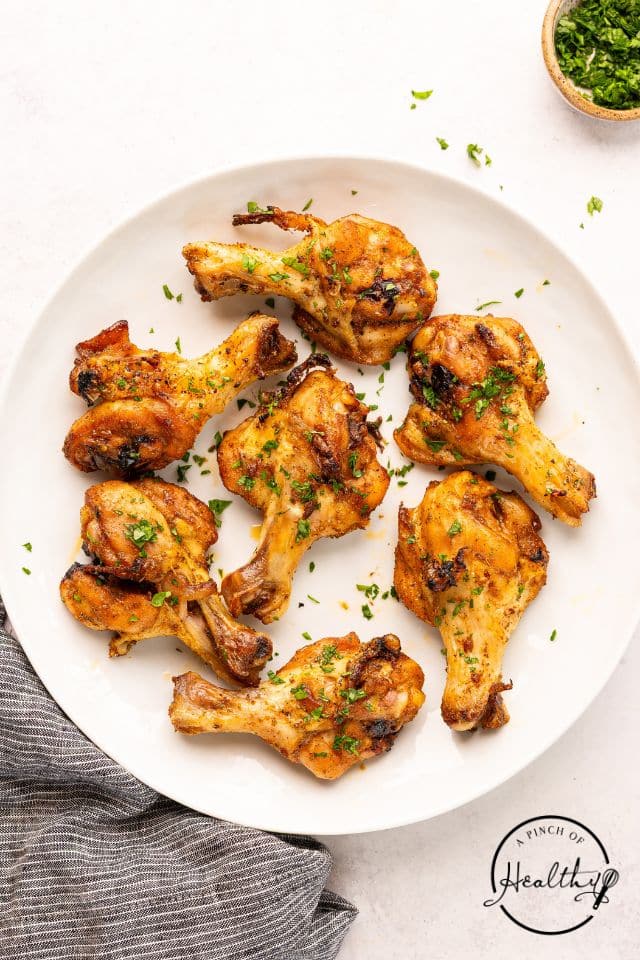 Cooked butterflied chicken legs on a white plate with parsley sprinkled on top.
