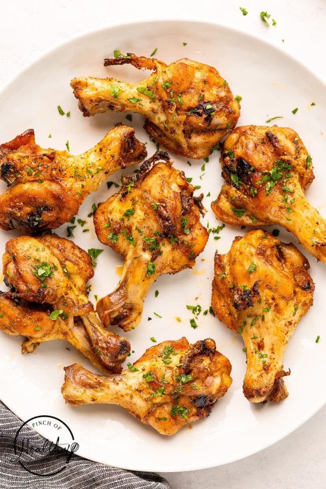 Butterflied chicken legs on a white plate garnished with fresh parsley.