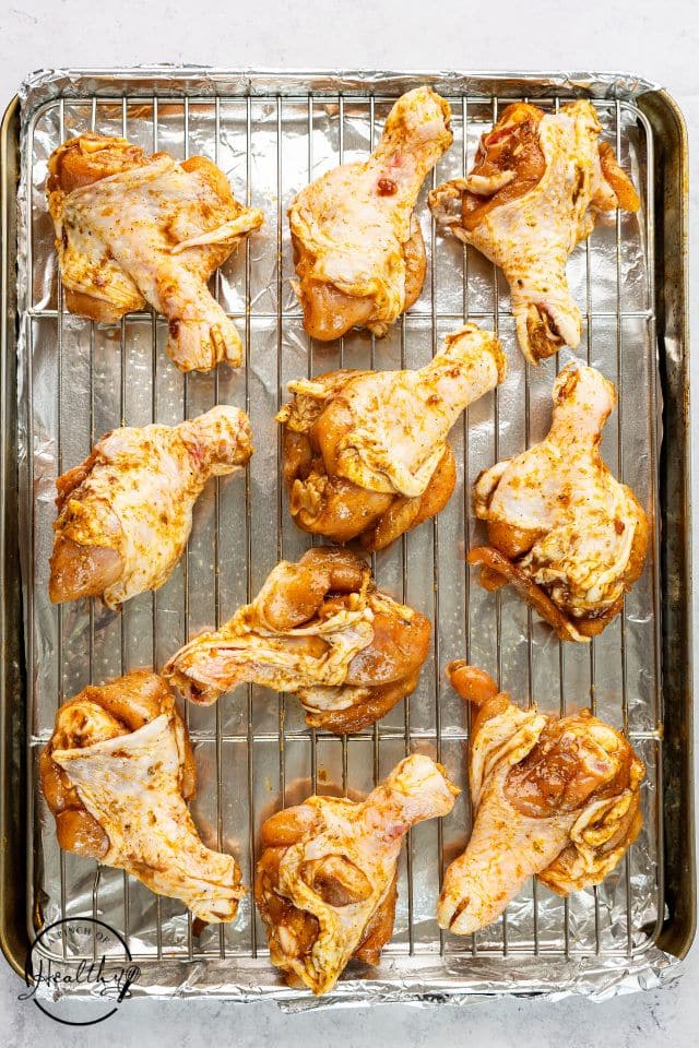 Marinated butterflied chicken legs on a wire pack placed over a baking sheet before being cooked.