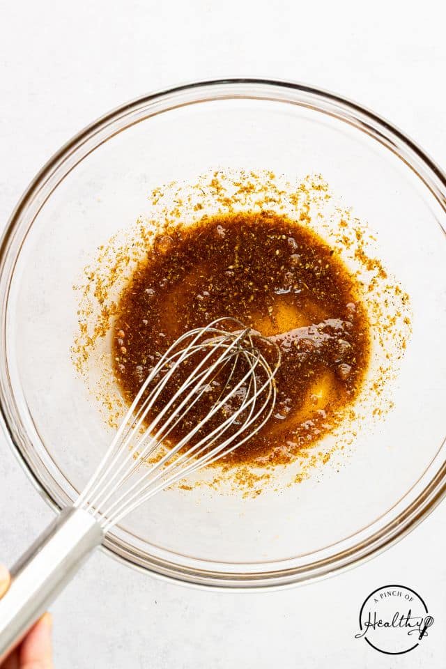 Marinade for butterflied chicken legs in a glass bowl with a whisk.