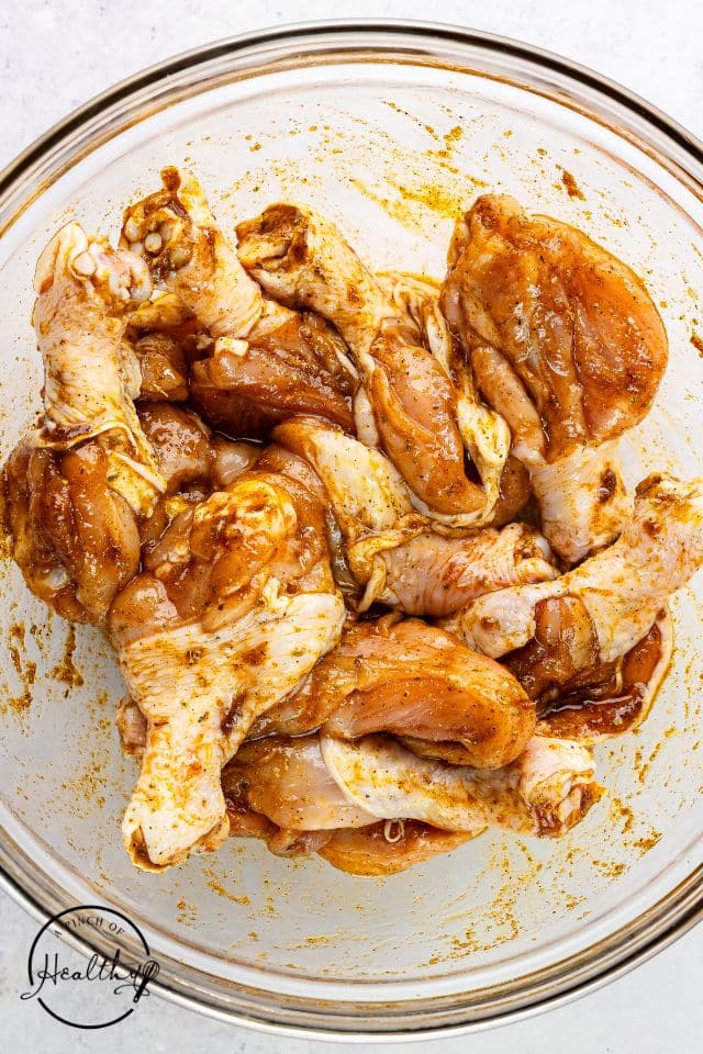 Butterflied chicken legs in a glass bowl after the marinade has been mixed in and evenly coated all sides of the chicken.