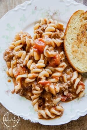 Hamburger casserole on a white textured plate with a slice of garlic bread
